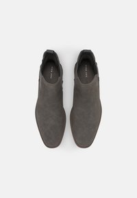 Bottes chevilles en daim gris avec un design élégant à bout pointu, panneaux latéraux élastiques et semelle marron texturée. Logo de la marque visible à l'intérieur.