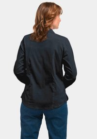 Black button-up shirt with a smooth texture, featuring long sleeves and a curved hem, paired with blue denim jeans.