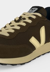 Gros plan d'une basket Veja marron avec des lacets beige, un logo beige sur le côté et une semelle beige clair sur fond blanc.