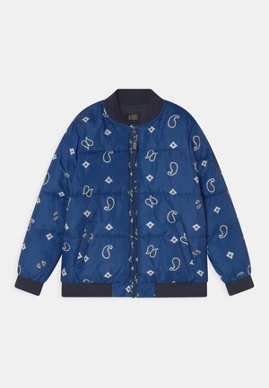 Niebieska pikowana kurtka zapinana na zamek, z czarnym kołnierzem i mankietami, kieszeniami po bokach oraz białymi wzorami paisley i geometrycznymi.