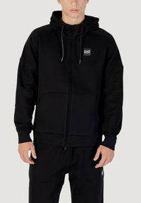 Schwarze Zip-Hoodie mit vorderer Tasche, verstellbarem Kordelzug-Kapuze und EA7-Logo-Patch auf der Brust. Hergestellt aus einem weichen, strukturierten Stoff.