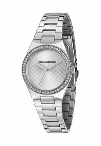 Silverfärgad klocka i rostfritt stål med fasetterad boett, strukturerad silverfärgad urtavla och kristalldetaljer runt ringen. Har ett länkarmband.