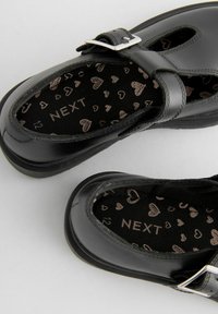 Chaussures en cuir noir avec un design Mary Jane, présentant une boucle sur le devant, une semelle intérieure texturée avec des motifs en forme de cœur et une forme de bout arrondi.