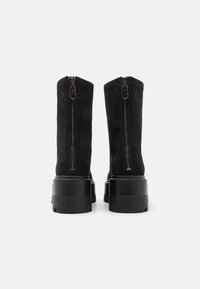 Par de botas negras de ante hasta la mitad de la pantorrilla con cremalleras traseras y suelas gruesas con plataforma grabadas con la marca Calvin Klein Jeans.