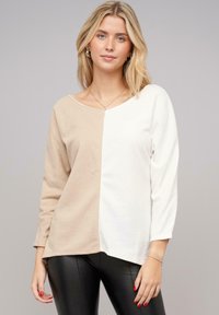 Crème en beige kleurblokkering lange mouw top met een brede halslijn. Zachte stof, ontspannen pasvorm en zijnaad detailing.