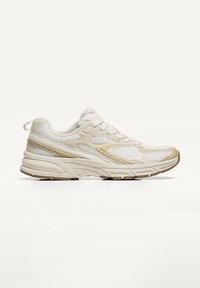 Scarpe sportive beige con tomaia in mesh, caratterizzate da dettagli dorati e colletto imbottito. La suola è spessa e testurizzata per un migliore supporto.