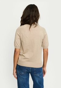 Pullover beige lavorato a maglia con maniche corte e orlo a coste, abbinato a jeans in denim blu. Tessuto liscio e design semplice e classico.