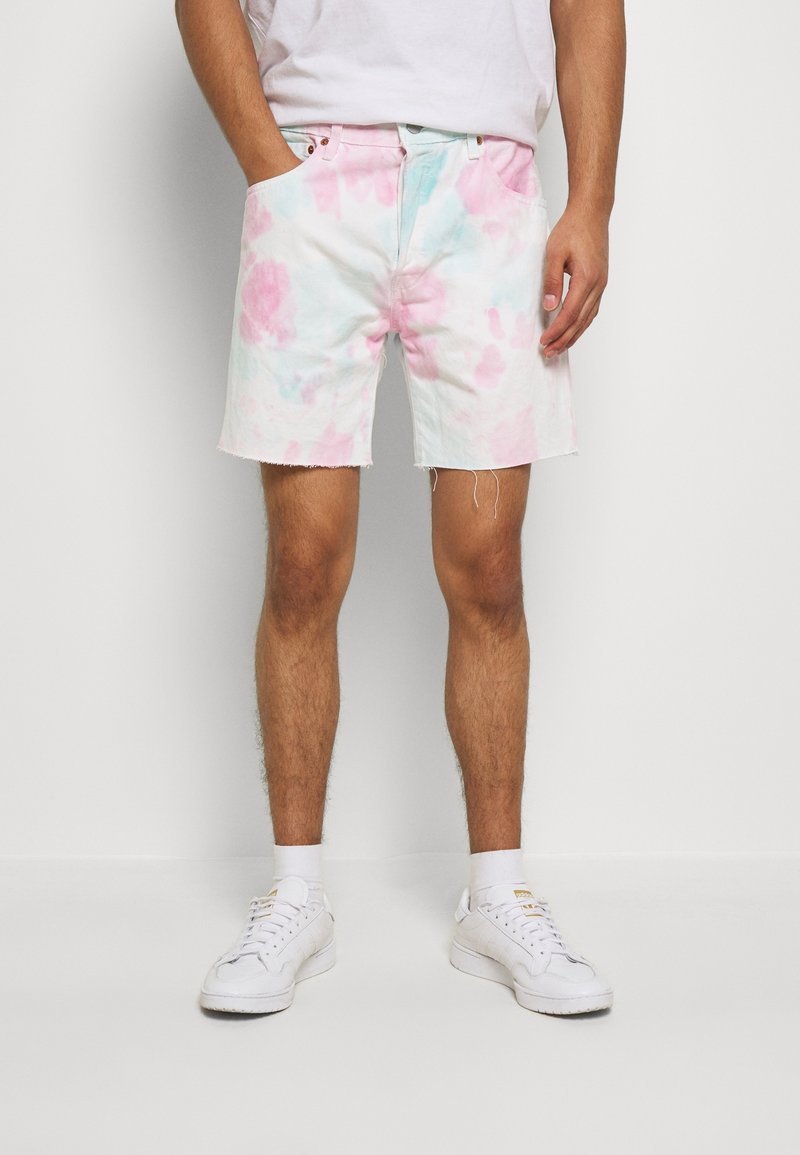 Shorts en denim à base blanche, ornés de motifs tie-dye rose et bleu, avec des bords effilochés et deux poches latérales. Stylés avec des baskets blanches.