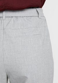Pantalon gris clair en tissu texturé avec une taille élastique et une poche arrière unique, conçu pour le confort et la facilité de port.