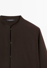 Brązowa koszula zapinana na guziki z stójką, charakteryzująca się gładką fakturą, subtelnymi detalami w szyciu oraz ciemnymi guzikami z przodu.