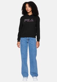 Felpa nera con un logo FILA prominente nei colori in degradé. Abbinata a jeans larghi azzurri e sneaker bianche.