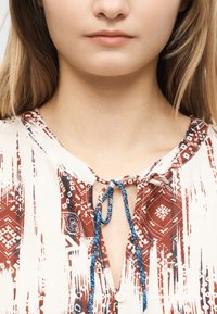 Κοντινή λήψη γυναίκας που φοράει πουκάμισο με σχέδιο και μπλε κορδόνι δεμένο στο λαιμό.