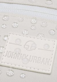 Világosszürke táska fényes, átlátszó kör alakú díszítésekkel és egy texturált címkével, amelyen világosan van feltüntetve a "JOHNNY URBAN" felirat.