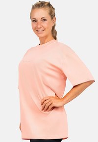 Lichtroze oversized t-shirt met korte mouwen, ronde halslijn en subtiele logo op de voorkant. Zachte textuur en relaxte pasvorm.