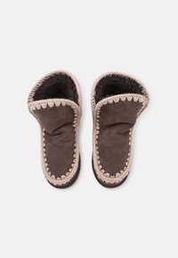 Pantofole in suede marrone con un morbido rivestimento in pelliccia scura, caratterizzate da un bordo intrecciato chiaro e un design aperto sulla parte superiore.