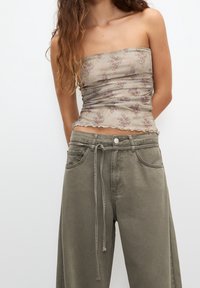 Haut bustier floral beige avec des fleurs lilas claires, côtés froncés et ourlet ondulé. Associé à un pantalon ample vert olive avec un cordon de serrage.