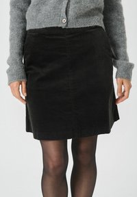 Zwarte corduroy rok met een getailleerde pasvorm, tot op de knie, met een gladde textuur en zijnaadzakken. Gekocht met een grijze gebreide cardigan.