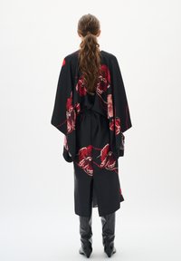 Rochie stil kimono neagră cu modele florale roșii, mâneci largi și o fanta în spate, asortată cu cizme negre înalte. Textură netedă.