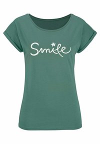 Zaļa T-krekls ar mīkstu tekstūru, noapaļotu apkakli, sarullētām piedurknēm un baltu "Smile" tekstu ar zvaigznītes akcentu.