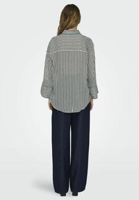 Camisa de cuadros en blanco y negro con yugo trasero, combinada con pantalones de mezclilla oscuros de pierna ancha. Mangas largas con detalle de puño.