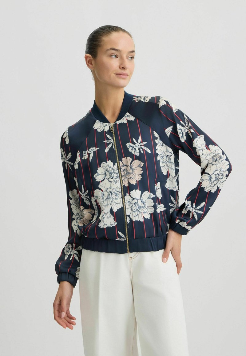 Chaqueta bomber de color azul marino con patrón floral blanco y franjas rojas, que cuenta con cierre de cremallera, cuello acanalado y puños y dobladillo elasticados.