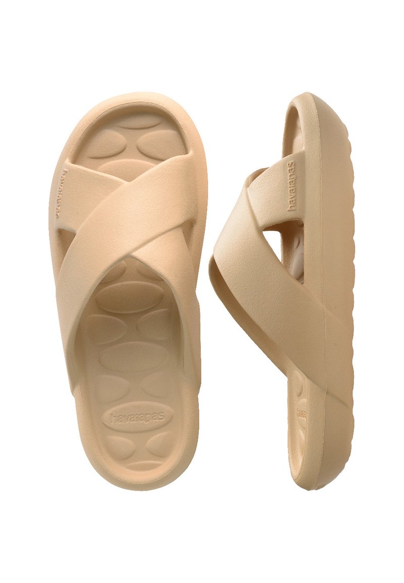 Beige cross-strap sandals made of flexible material; textured footbed with oval patterns; contoured sole for comfort.