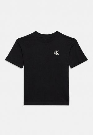 T-shirt noir à manches courtes et col rond, avec un petit logo CK blanc sur la poitrine, présenté sur un fond uni clair.