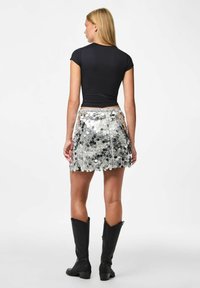 Zwarte getailleerde top en een glanzende zilveren pailletten minirok met een franjeszoom. Kniehoge zwarte cowboylaarzen maken de look compleet.
