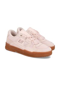Een paar lichtroze sneakers van het merk DC met geperforeerde zijkanten, meshpanelen en bruine rubberen zolen, getoond onder een lichte hoek op een witte achtergrond.
