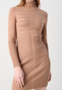 Robe en tricot beige clair, avec un col polo, une texture à côtes verticales et des rayures horizontales sur la partie supérieure.