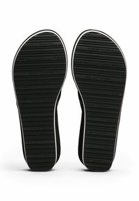 Suelas de zapatos de goma negra con textura antideslizante y logotipo en relieve. Finas líneas blancas a lo largo de los bordes, forma curva en el talón y la punta.