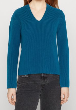 Morski sweter z prążkowanego dzianiny z dekoltem w serek i długimi rękawami, noszony z czarnymi, wysokim stanem, jeansami, widoczny od szyi do bioder.