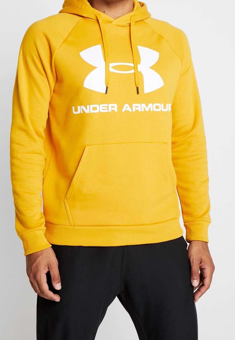Sudadera amarilla con un bolsillo tipo canguro y puños acanalados. Presenta un gran logotipo blanco de Under Armour en la parte frontal. Material suave de mezcla de algodón.