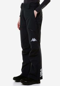Pantaloni da neve neri con cerniere sulle tasche, logo Kappa sulla coscia, vita regolabile, vestibilità dritta e testo "USA" sulla parte inferiore della gamba.