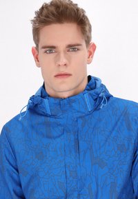 Giacca blu con un motivo geometrico, dotata di cappuccio, chiusura con cerniera e dettagli con coulisse. Texture liscia con un design leggero.