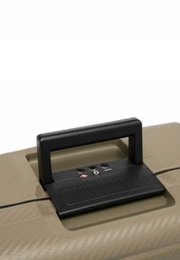 Valigia rigida di colore beige chiaro, dotata di una maniglia nera e di un pannello di controllo con tre porte e una superficie texturizzata per una migliore presa.