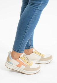 Zapatillas con una parte superior blanca, acentos en beige y azul pastel, con un cuello acolchado y una suela texturizada. Presenta un detalle de cuero melocotón en el lateral.