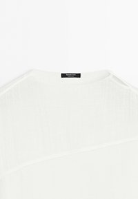 Bílá lněná košile s černým štítkem Massimo Dutti na vnitřní části výstřihu, zobrazená zezadu na jednobílém pozadí.