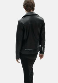 Black leather jacket with a structured design, wide collar, and stitched detailing. Zippered accent at the cuff, sleek and fitted silhouette.