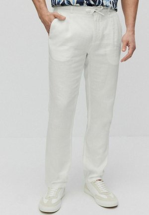 Witte linnen broek met een relaxte pasvorm, voorzien van zijzakken en een trekkoord tailleband, gecombineerd met witte sportschoenen.