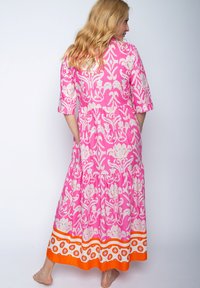 Rosa Maxi-Kleid mit weißen floralem Muster, kurzen Ärmeln, einem gestuften Rock und einem orange-weiß gemusterten Saum. Der Stoff wirkt leicht.