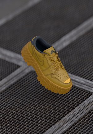 Żółty sneaker Nike Air z grubą, teksturowaną podeszwą unoszący się nad metalową siatką podłogową, pokazujący widoki boczne i z góry z wiązanymi sznurowadłami.