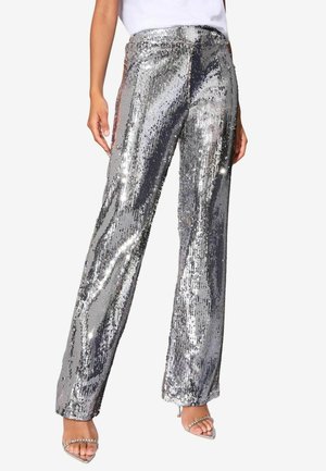 Pantalones de pierna ancha plateados con lentejuelas, de textura suave y acabado brillante, que cuentan con una cintura alta y un ajuste holgado. Combinados con tacones transparentes.