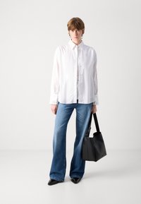 Hvit langermet skjorte med knapper, blå flare jeans og svart skinnveske. Glatt stoff, skreddersydd passform, minimalistisk design. Sorte spissede sko.