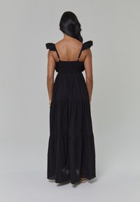 Czarna maxi sukienka z warstwowymi falbanami, marszczoną górą i ozdobnymi ramiączkami z falbanami. Wykonana z lekkiego materiału, z odsłoniętymi plecami.
