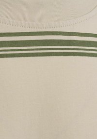 Tejido de punto beige con una textura suave que presenta tres finas franjas verdes horizontales cerca del escote. Diseño básico y ajustado.