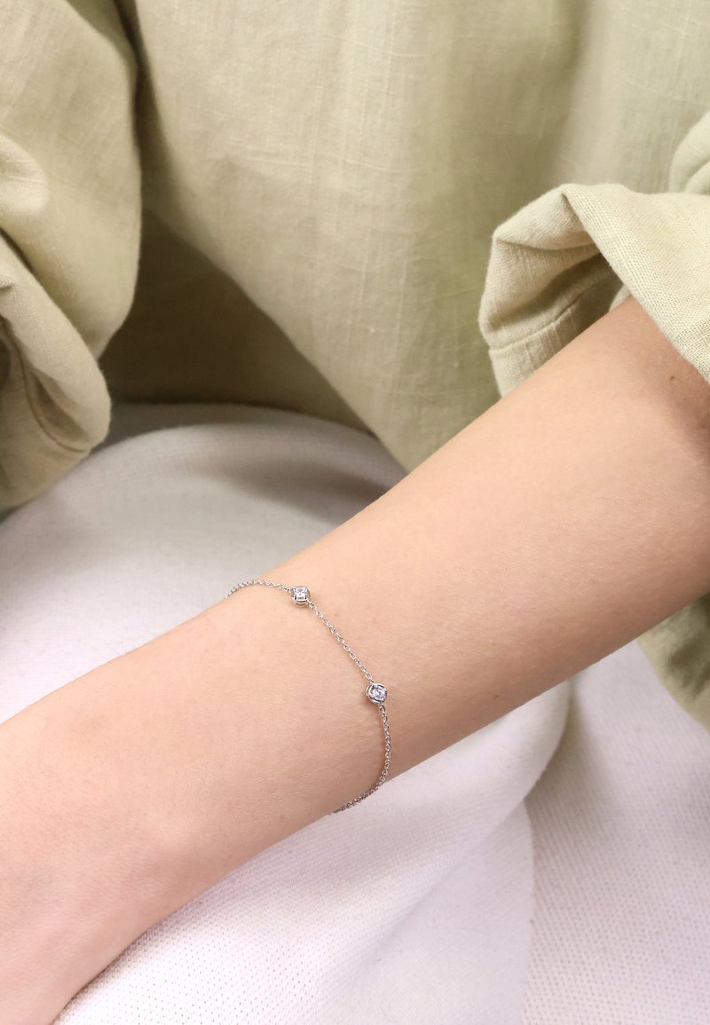 Silver chain bracelet featuring three clear, square gemstones set at intervals. Smooth texture with a minimalist design.