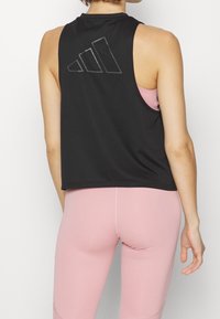 Top atlético sin mangas negro con un acabado texturizado, presentando tres rayas en relieve en la parte posterior. Combinado con leggins rosas claros.