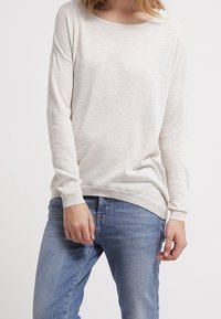 Ljusbeige långärmad tröja med rund halsringning. Har en mjuk textur och ribbade manschetter, ihop med blå denimjeans.