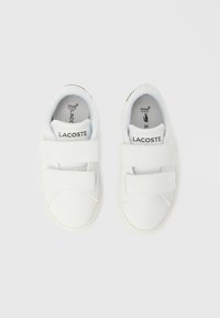 Λευκά παπούτσια με διπλούς ιμάντες Velcro και στρογγυλεμένη μύτη. Κατασκευασμένα από λείο υλικό, με μαύρο λογότυπο της μάρκας στο λουράκι και στη σόλα.